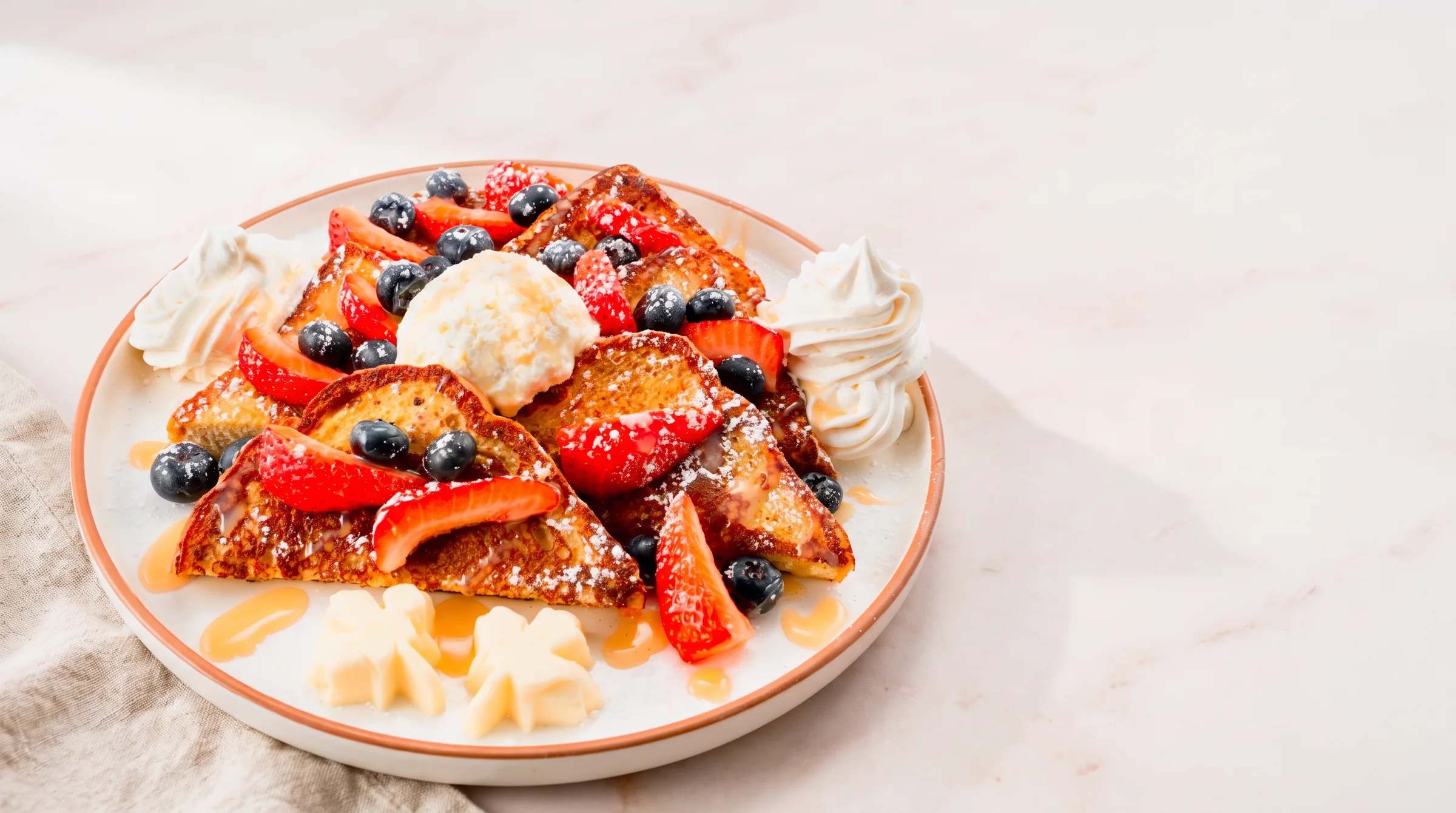 Griddled French toast topped with a scoop of lemon ricotta, fresh strawberries & blueberries, dusted with powdered sugar, and a Ghirardelli vanilla sauce, Served with our signature maple butter